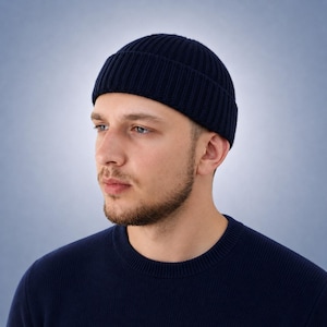 May include: A dark navy blue beanie with a ribbed knit texture and a folded cuff. The beanie is constructed from a solid-colored yarn and features a rounded crown that fits closely to the head, providing a simple and functional head covering.