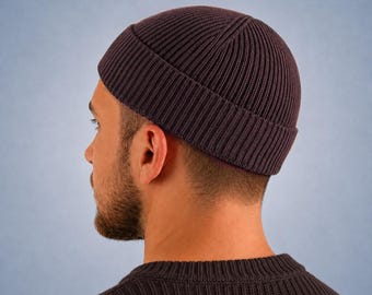 May include: A dark brown, ribbed knit beanie cap with a folded cuff. The hat features a vertical textured pattern throughout the fabric, providing a snug fit around the head. The material appears to be a soft, woven textile in a solid dark brown color.