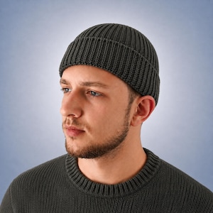 May include: A dark charcoal gray knit beanie with a thick ribbed texture and a folded cuff. The beanie is constructed from a dense, vertical knit pattern that provides a structured fit, covering the crown of the head with a clean, rounded silhouette.
