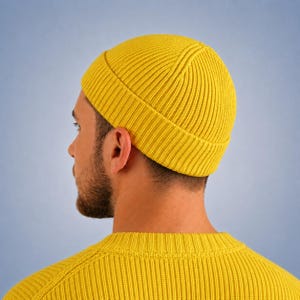 May include: A bright yellow beanie with a thick ribbed knit texture and a wide folded cuff. The hat is worn on the head, showcasing the vertical knit pattern that extends from the crown down to the brim, providing a consistent look.