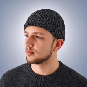 May include: A dark charcoal grey ribbed knit beanie hat with a folded cuff edge. The hat features a vertical textured knit pattern throughout the crown and a thick, double-layered brim that sits snugly around the head for a classic fit.