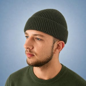 May include: A dark olive green ribbed knit beanie with a folded cuff. The hat features a vertical textured pattern throughout the fabric, providing a consistent look from the crown down to the thick, structured brim that sits above the ears.