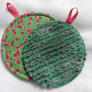 May include: Two round pot holders. One is green with a textured surface and the other is green with a watermelon print. Both have pink fabric loops.