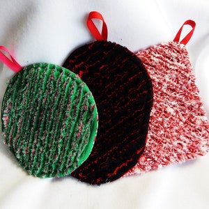 May include: Three round pot holders with red, black, and green fabric. Each pot holder has a loop for hanging.