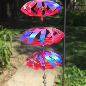 Puede incluir: Un carillón de viento iridiscente rosa y azul con tres niveles de círculos superpuestos y un colgante de cristal en forma de lágrima.