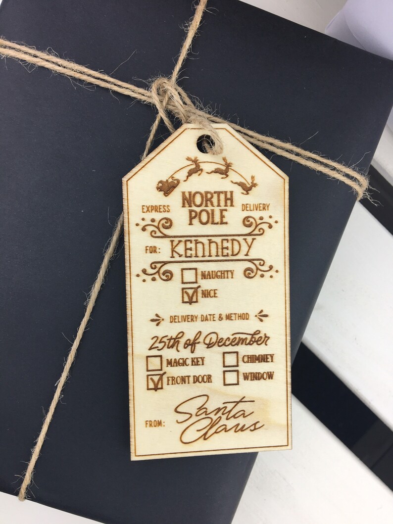 May include: A wooden Christmas gift tag with a North Pole Express theme. The tag is decorated with a reindeer and sleigh, and has a checklist for Santa Claus to fill out. The tag is addressed to Kennedy and includes a delivery date of December 25th. The tag is from Santa Claus.