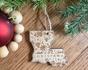 May include: A wooden ornament shaped like the state of Louisiana with a floral design and the word "LOUISIANA" inscribed on it.