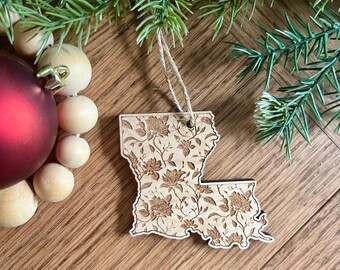 May include: A wooden ornament shaped like the state of Louisiana with a floral pattern. The ornament is hanging from a twine string.