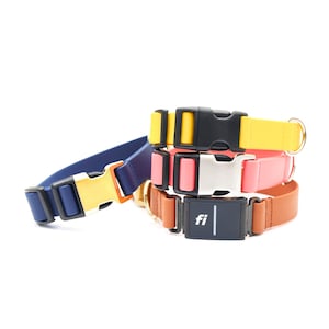 May include: A stack of four dog collars in different colors, including yellow, pink, blue, and brown. The top collar has a black buckle and a small black device with the text "fi" on it.