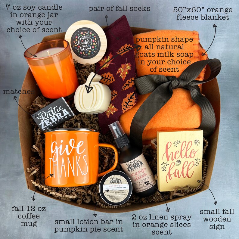 May include: An orange gift basket filled with fall-themed items. Includes a 7 oz soy candle, a 50"x60" orange fleece blanket, a coffee mug with "Give Thanks" text, a small wooden sign, and other scented products.