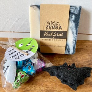 May include: A Halloween-themed gift set featuring a bar of "black forest" handmade soap, a small bag of wrapped candies, and a felt bat decoration. The soap has a brown label with the shop's name and the words "black forest".
