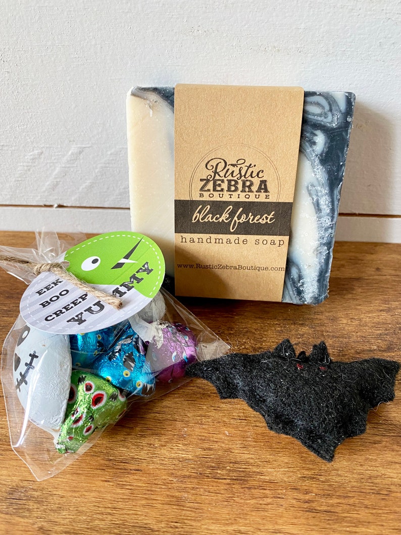 May include: A Halloween-themed gift set featuring a bar of "black forest" handmade soap, a small bag of wrapped candies, and a felt bat decoration. The soap has a brown label with the shop's name and the words "black forest".