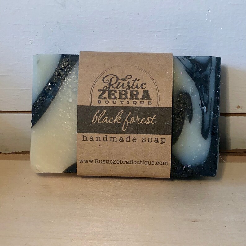 May include: A bar of handmade soap with a black and white swirl design. The soap is labeled "Rustic Zebra Boutique" and "black forest".