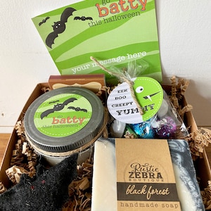 May include: A Halloween-themed gift box with a green and black bat design. The box contains a jar with a bat label, a bar of black forest handmade soap, a small bag of treats, and a card that says "go batty this halloween".