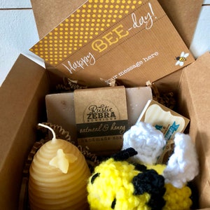 May include: A gift box filled with bee-themed items, including a honey-scented candle shaped like a honeycomb, a crocheted bee toy, a bar of oatmeal and honey soap, and a card that says "Happy Bee-day!"