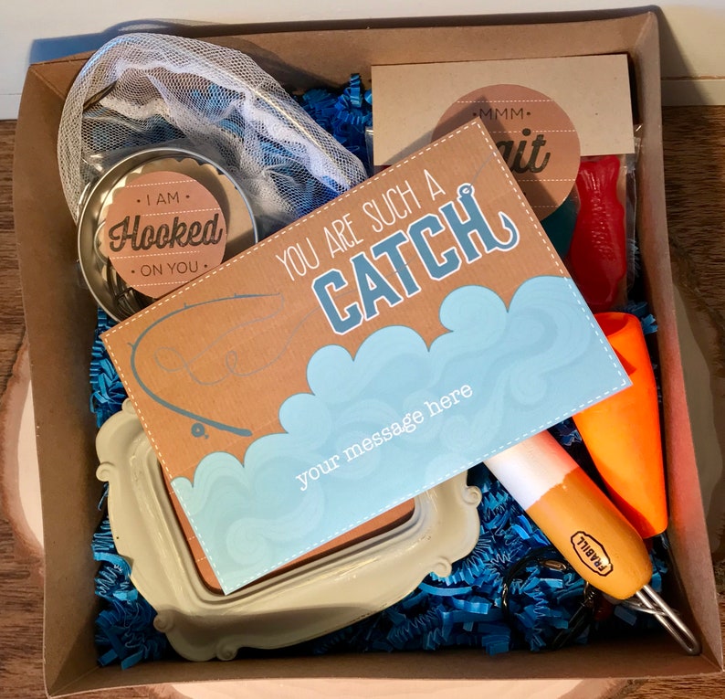 Puede incluir: Una caja de regalo llena de art&iacute;culos con tem&aacute;tica de pesca, que incluyen una red, un peque&ntilde;o frasco con una etiqueta que dice "I am Hooked on You", una tarjeta que dice "You are such a Catch", un se&ntilde;uelo de pesca y una bolsa de gusanos rojos gomosos.