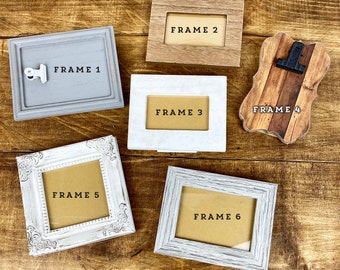 May include: Six different picture frames in various styles and colors, including white, gray, and wood. The frames are arranged on a wooden surface. The text "FRAME 1", "FRAME 2", "FRAME 3", "FRAME 4", "FRAME 5", and "FRAME 6" is visible on the frames.