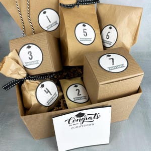 May include: A graduation countdown gift set with brown paper bags and boxes, each labeled with a number and "Days Left" on a white circle. A card with "Congrats" and "Countdown" is in the front.