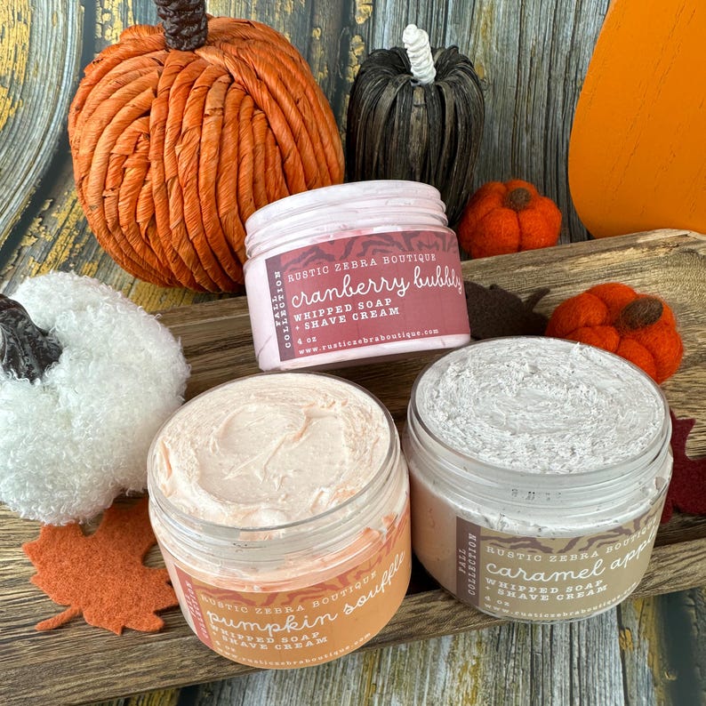 May include: An arrangement of fall-themed products, including decorative pumpkins and jars of whipped soap and shave cream. The jars are labeled with flavors like "cranberry bubbly" and "pumpkin souffl&eacute;". The image has a warm, autumnal color palette.