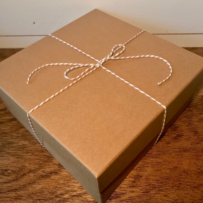 Op de afbeelding: Een bruine kartonnen doos gebonden met wit en bruin touw. De doos is ingepakt in bruin papier en heeft een eenvoudige, rustieke uitstraling.