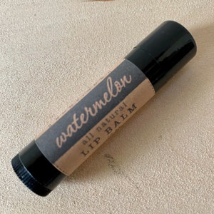 May include: A black lip balm tube with a brown paper label that says "watermelon all natural LIP BALM".