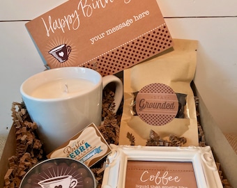 May include: A brown gift box filled with a coffee-themed birthday gift set. The set includes a white mug with a candle inside, a bag of coffee beans with a "Stay Grounded" label, a small tin of chocolate coffee beans, a small framed sign that says "Coffee liquid that smells like fresh ground heaven", and a card that says "Happy Birthday" with space for a message.
