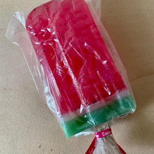 May include: A watermelon-shaped soap bar wrapped in clear plastic with a pink ribbon tied around it. The ribbon has the text "Especially for you" printed on it.