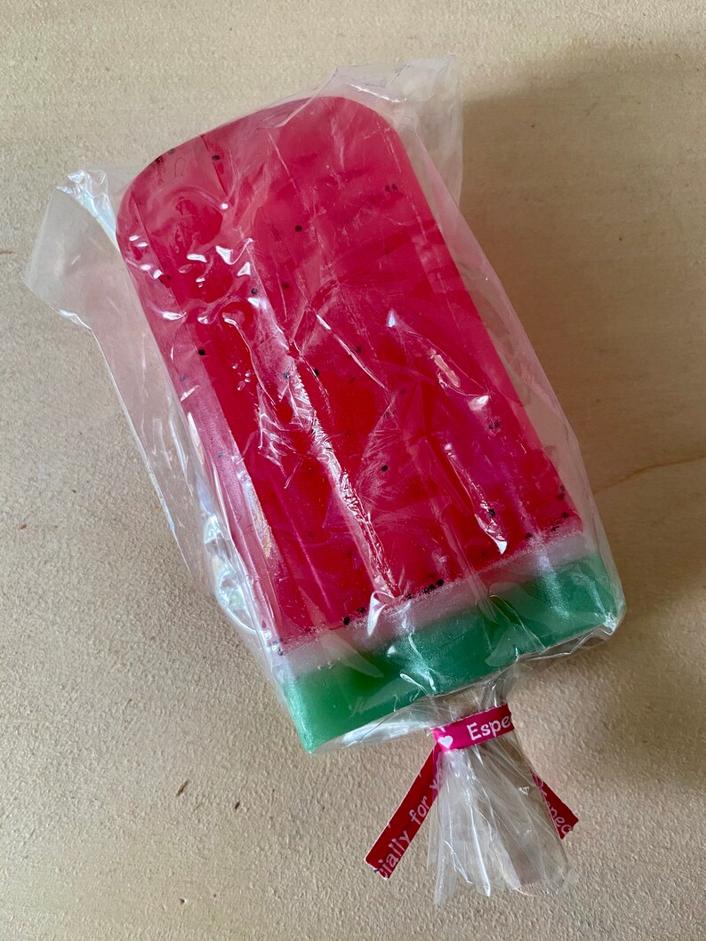 May include: A watermelon-shaped soap bar wrapped in clear plastic with a pink ribbon tied around it. The ribbon has the text "Especially for you" printed on it.