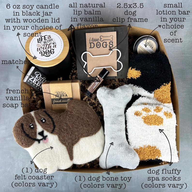 May include: A gift box filled with dog-themed items, including a 6 oz soy candle, a lip balm, a dog bone toy, a dog felt coaster, a dog clip frame, a bar of soap, and a pair of dog spa socks. The box is filled with brown shredded paper. The candle has a label that says "Life is better with a dog". The lip balm is in a small tube with a label that says "Vanilla". The dog bone toy is white with brown paw prints. The dog felt coaster is brown and white and shaped like a dog. The dog clip frame is black with a white bone-shaped frame. The bar of soap is white with a label that says "French Vanilla". The dog spa socks are white with brown paw prints. The box is decorated with a brown ribbon.