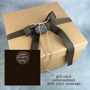 May include: A brown gift box tied with a dark brown ribbon and a decorative tag. The tag reads "Grateful, thankful, and blessed" surrounded by colorful leaves and flowers. A gift card is included.