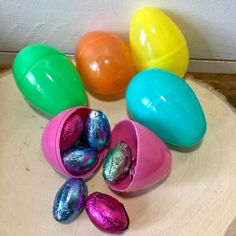May include: A collection of colorful plastic Easter eggs with a variety of chocolate candies inside. The eggs are in shades of green, blue, orange, and yellow. The candies are wrapped in foil and have different colors and designs.