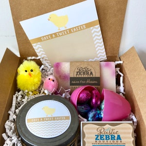 May include: A gift box filled with Easter-themed items, including a jar of hand cream with a "Have a Tweet Easter" label, a pink plastic egg filled with chocolate candies, two bars of soap with a "Rustic Zebra Boutique" label, and two yellow chick toys.