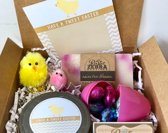 May include: A gift box filled with Easter-themed items, including a jar of hand cream with a "Have a Tweet Easter" label, a pink plastic egg filled with chocolate candies, two bars of soap with a "Rustic Zebra Boutique" label, and two yellow chick toys.