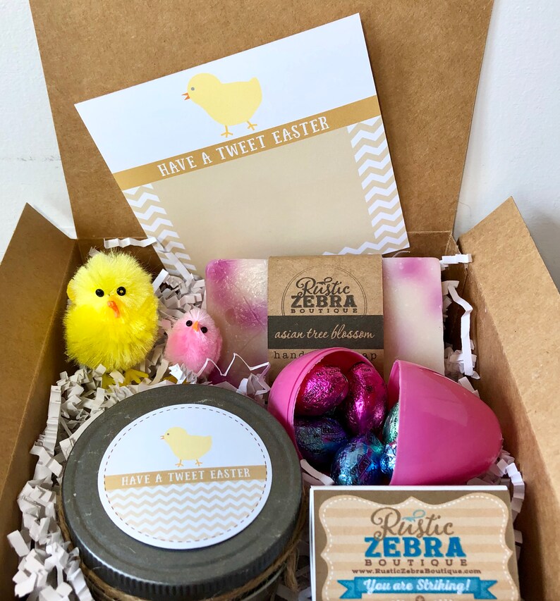 May include: A gift box filled with Easter-themed items, including a jar of hand cream with a "Have a Tweet Easter" label, a pink plastic egg filled with chocolate candies, two bars of soap with a "Rustic Zebra Boutique" label, and two yellow chick toys.