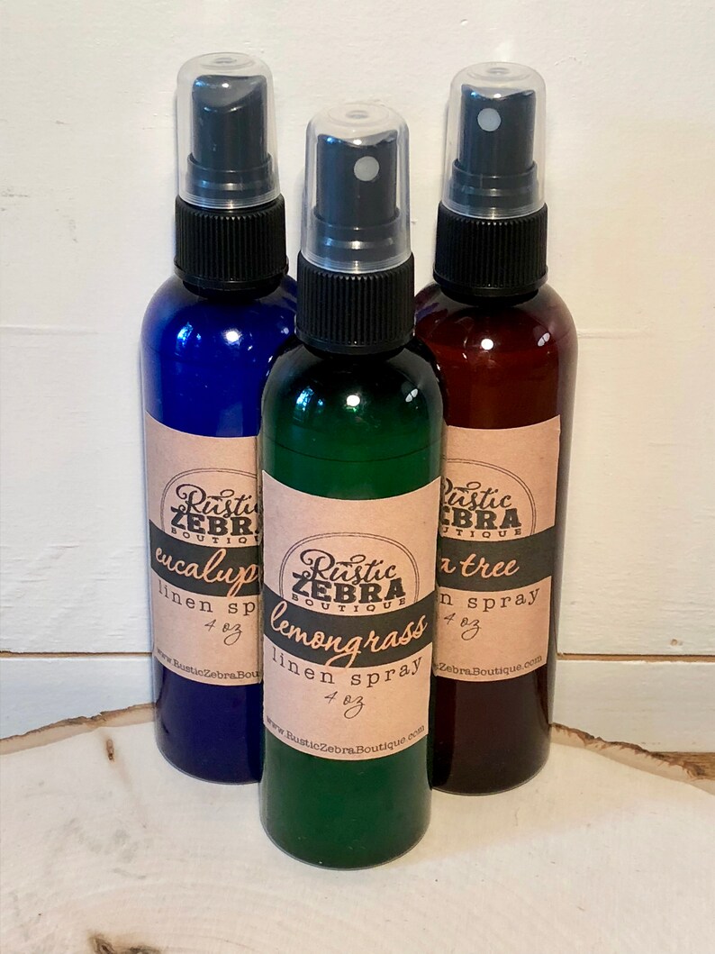 May include: Three linen spray bottles in blue, green, and brown. Each bottle has a black spray nozzle and a label with the text "Rustic Zebra Boutique" and the scent name: eucalyptus, lemongrass, and tea tree. Each bottle is 4 oz.
