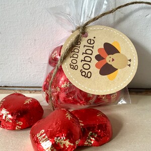 May include: A clear cellophane bag tied with twine, containing heart-shaped candies wrapped in red foil. A round tag with the words "gobble. gobble." and a turkey illustration is attached.