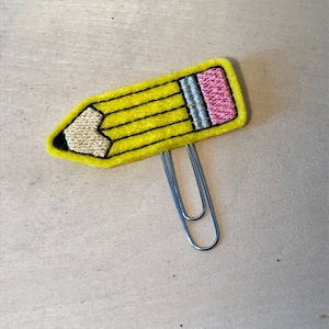 May include: A yellow felt pencil clip with a pink eraser and a silver paper clip.