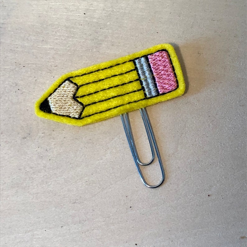 May include: A yellow felt pencil clip with a pink eraser and a silver paper clip.