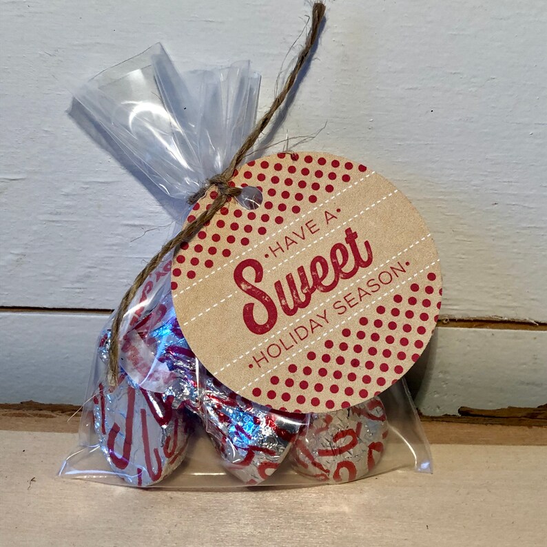 May include: A clear plastic bag filled with foil-wrapped chocolate candies tied with twine and a round gift tag. The tag is brown with red polka dots and the text "Have a Sweet Holiday Season."