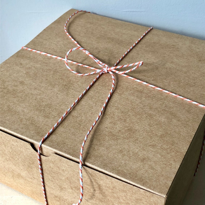 May include: A brown cardboard box tied with a decorative string. The string is white, orange, and brown, forming a bow on top. The box is closed and ready for gifting.