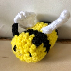 May include: A crocheted bee toy with yellow and black stripes, white wings, and black eyes.