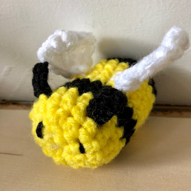 May include: A crocheted bee toy with yellow and black stripes, white wings, and black eyes.