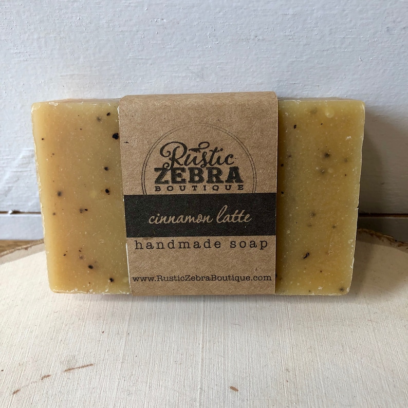 Puede incluir: Una barra de jab&oacute;n artesanal de canela y latte con una etiqueta de papel marr&oacute;n que dice "Rustic Zebra Boutique" y "jab&oacute;n artesanal de canela y latte", junto con la direcci&oacute;n del sitio web "www.RusticZebraBoutique.com".