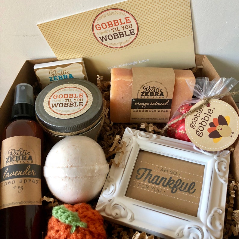 May include: A gift box filled with various items, including a lavender linen spray, orange oatmeal handmade soap, a bath bomb, and a decorative frame with the text "I AM SO Thankful FOR YOU." The box also contains a card that says "GOBBLE TIL YOU WOBBLE."