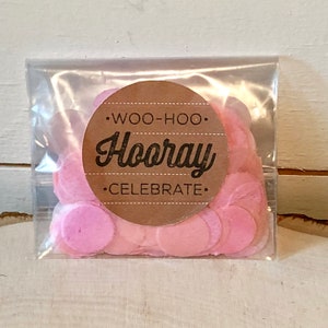 Op de afbeelding: Een doorzichtige plastic zak gevuld met roze papieren confetti. De zak heeft een bruine ronde sticker met de tekst "Woo-hoo! Hooray Celebrate."