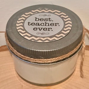 May include: A small glass jar with a silver lid and a brown twine bow. The lid has a white and gray chevron patterned sticker with the text "best. teacher. ever."