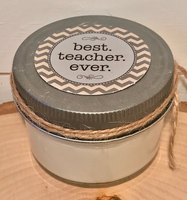May include: A small glass jar with a silver lid and a brown twine bow. The lid has a white and gray chevron patterned sticker with the text "best. teacher. ever."