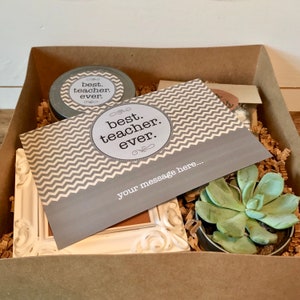 May include: A gift box filled with a small succulent plant, a white picture frame, a jar of candle, and a card with the text "best. teacher. ever." on a gray chevron background. The card also has the text "your message here..." printed on it.