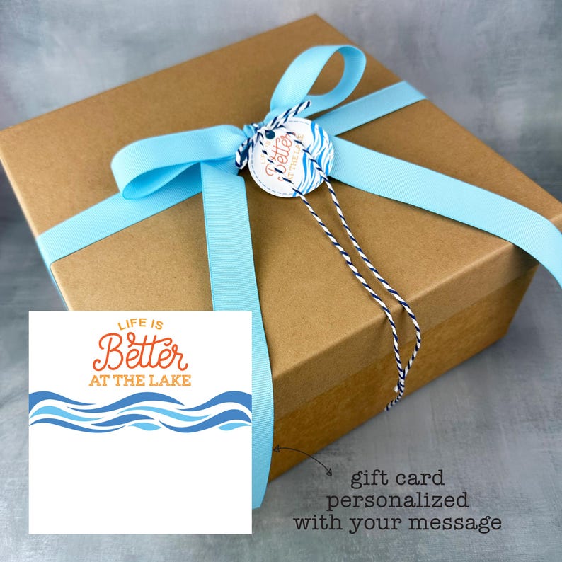May include: A brown gift box tied with a light blue ribbon and a matching tag. The tag reads "Better at the Lake" and is attached with twine. A card with the text "Life is Better at the Lake" is also included.