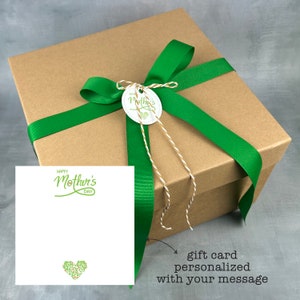 May include: A brown gift box tied with a green ribbon and a tag that says "Mother's Day". A white card with the words "Happy Mother's Day" is also included. The gift box is ready to be given as a present.